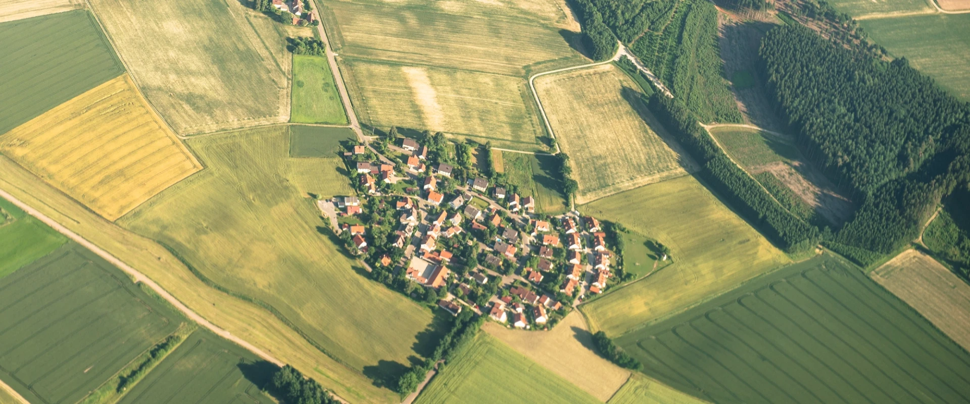 Luftaufnahme eines kleinen Dorfes umgeben von landwirtschaftlichen Feldern und Wäldern