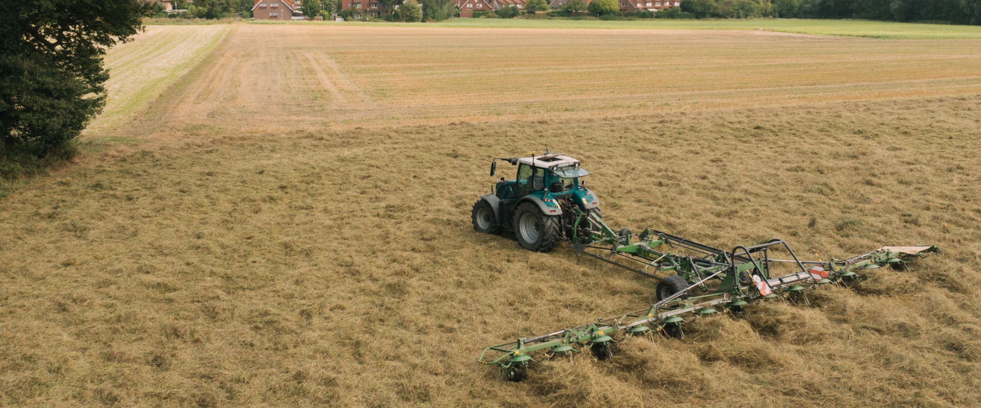 Traktor auf einem Feld bei der Arbeit, nahe eines kleinen Dorfes