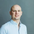 Portrait of a bald man in a light blue shirt against a grey background