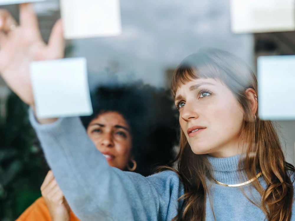 Two women looking through a glass wall covered with sticky notes
