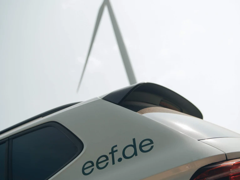 Nahaufnahme des Dachs eines Autos mit der Aufschrift 'eef.de', im Hintergrund eine unscharfe Brückenkonstruktion