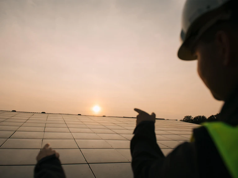 Ingenieur in Schutzhelm und Sicherheitsweste zeigt auf Solarmodule bei Sonnenuntergang