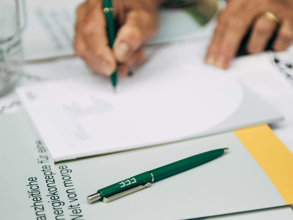 Person schreibt auf ein Blatt Papier neben einem grünen Stift