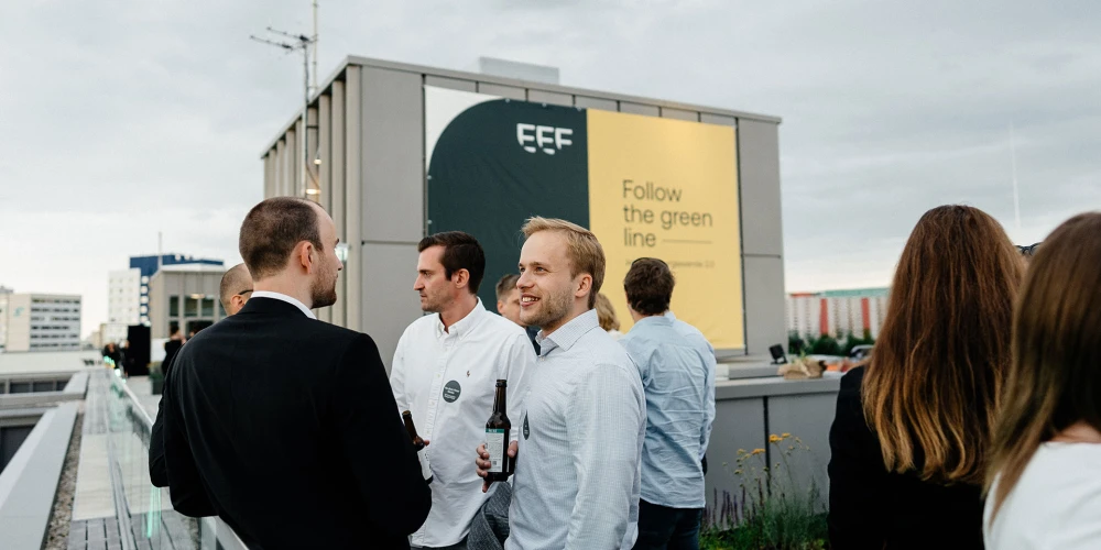 Gruppe von Personen bei einem Networking-Event auf einer Dachterrasse mit städtischer Kulisse im Hintergrund