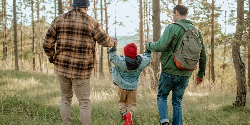 Zwei Männer und ein Kind halten Hände und laufen durch einen Wald