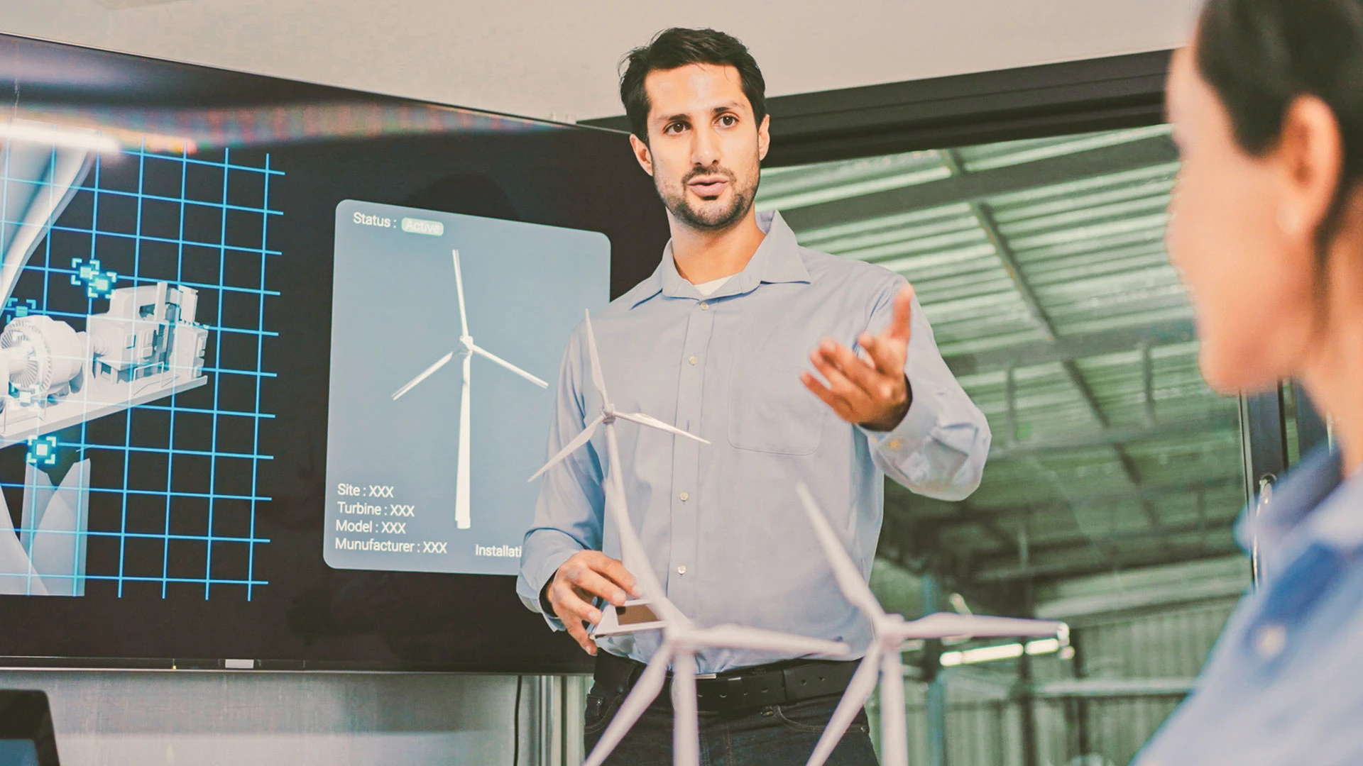 A man presenting wind power technology on a screen in a meeting room with two listeners