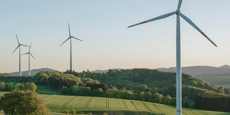 Windräder in einer grünen Hügellandschaft bei Sonnenuntergang