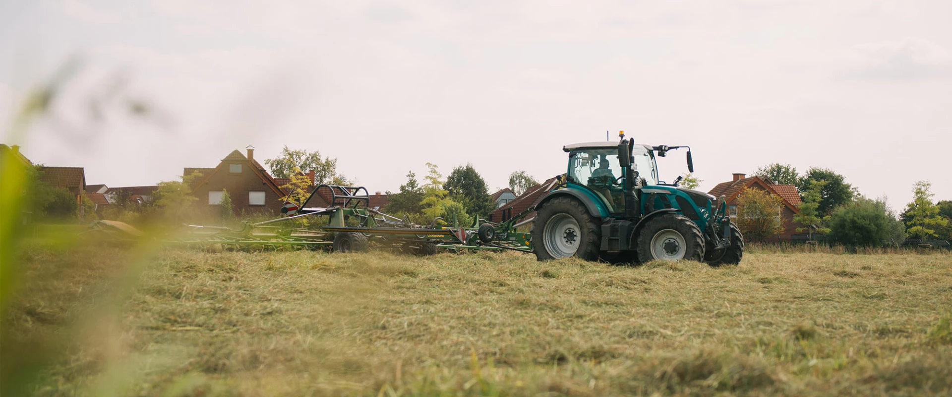 Tractor mowing grass in a field near some houses