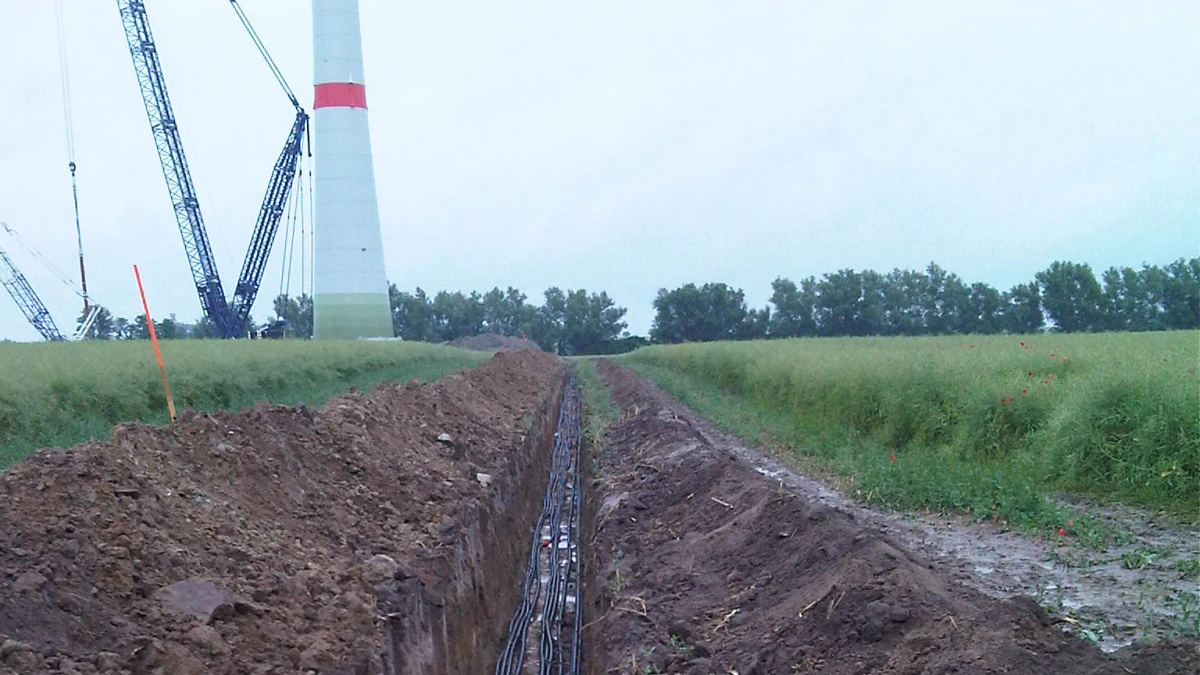 Erdgraben mit Kabeln am Fuße eines Windrades auf einem Feld