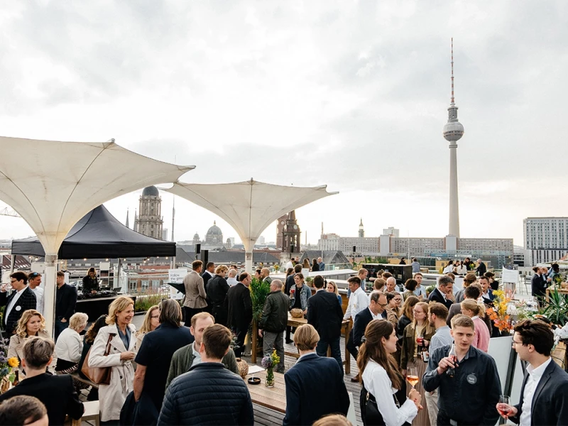 Menschen bei einer gesellschaftlichen Veranstaltung auf einer Dachterrasse mit Blick auf die Berliner Skyline, einschließlich des Fernsehturms