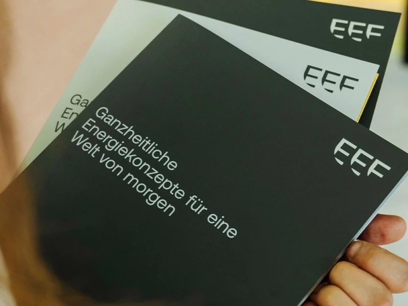 Person hält Broschüren mit dem Logo 'EEF' und dem Text 'Ganzheitliche Energiekonzepte für eine Welt von morgen'