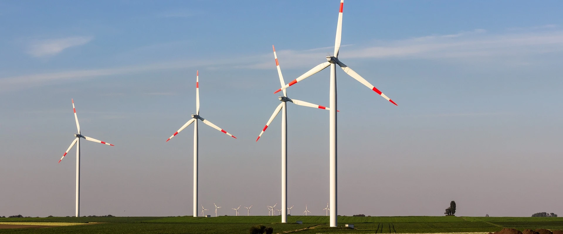 Three wind turbines on a harvested field under a blue sky