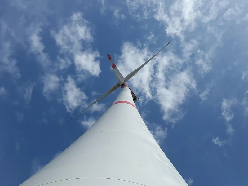 Blick von unten auf ein Windrad gegen einen blauen Himmel mit Wolken
