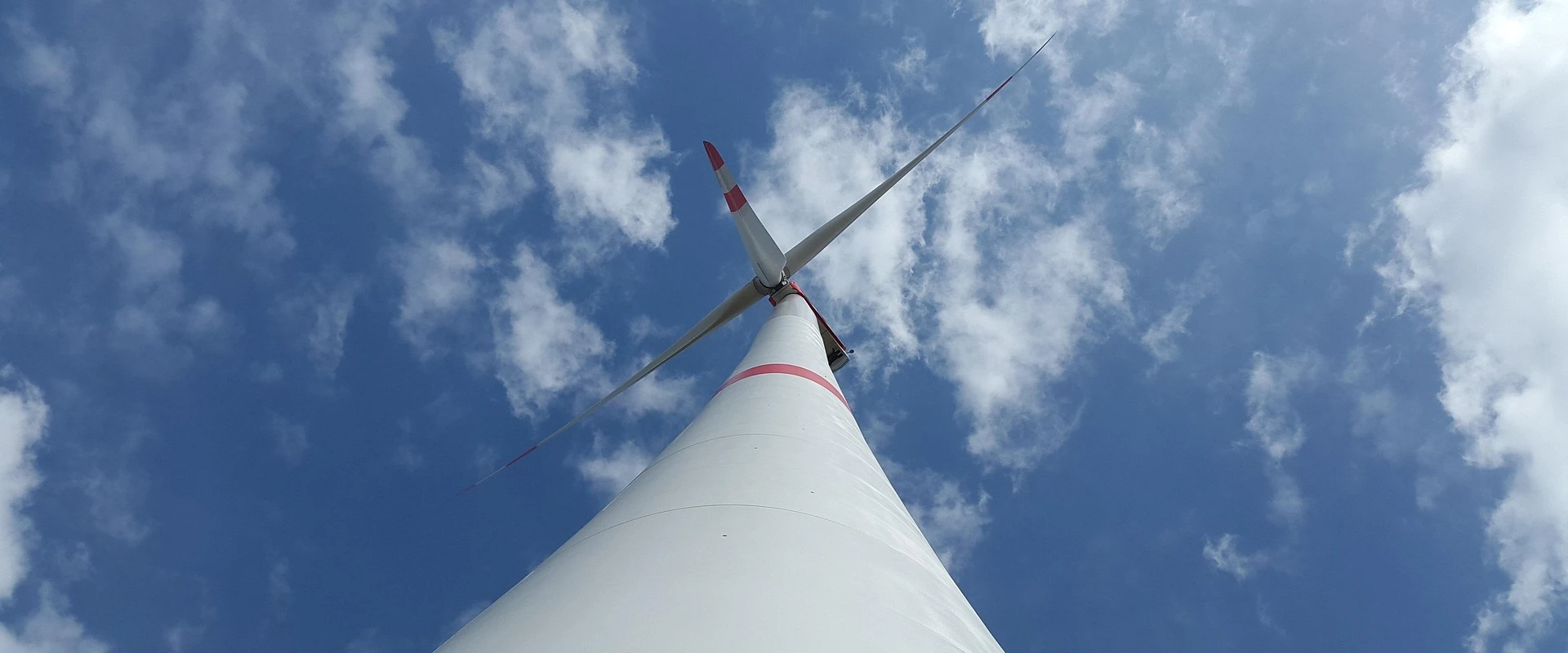 Blick von unten auf ein Windrad gegen einen blauen Himmel mit Wolken