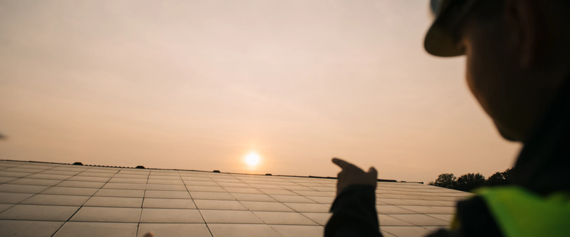 Engineer in safety gear pointing at solar panels at sunset