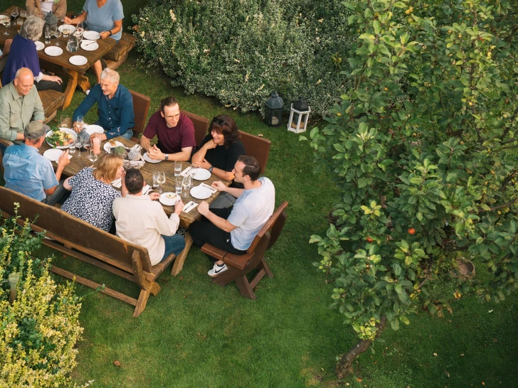 Gruppe von Menschen, die im Garten um einen Tisch sitzen und zusammen essen