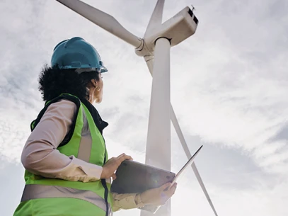 Ingenieurin mit Helm und Sicherheitsweste überprüft Windkraftanlage mit Tablet