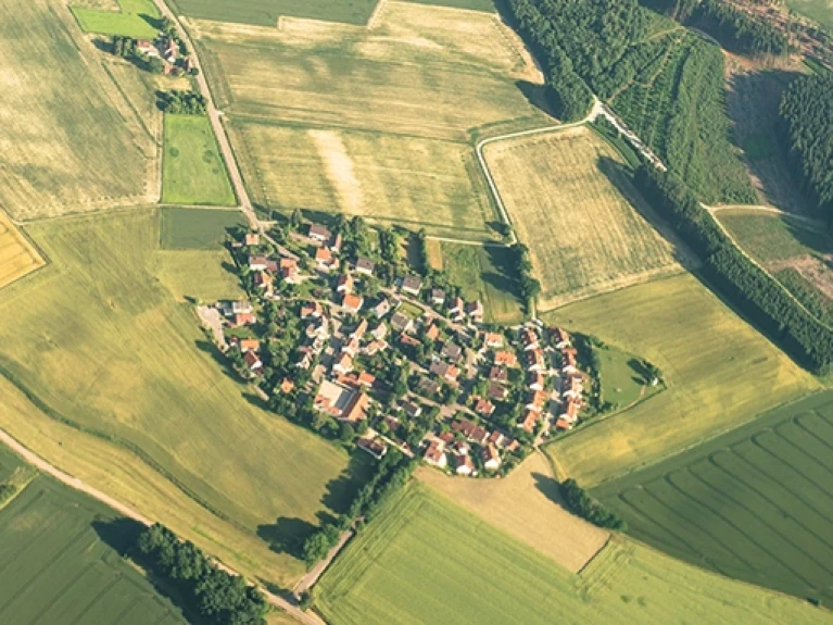 Luftaufnahme eines kleinen Dorfes umgeben von landwirtschaftlichen Feldern und Wäldern