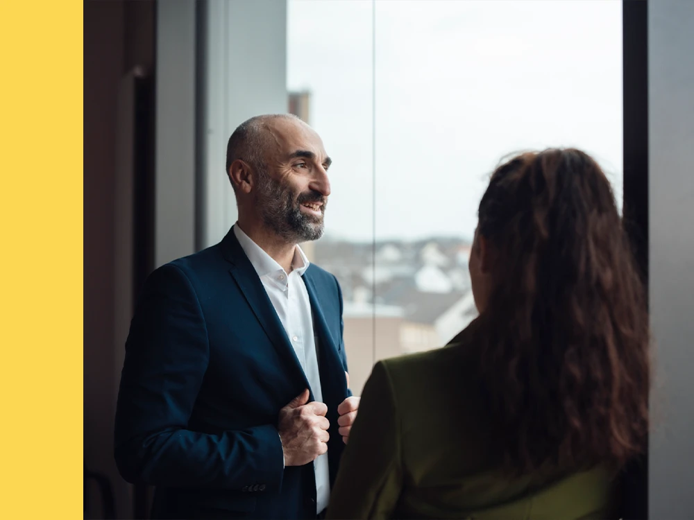 Bald man in a suit talking to a woman, seen from the back