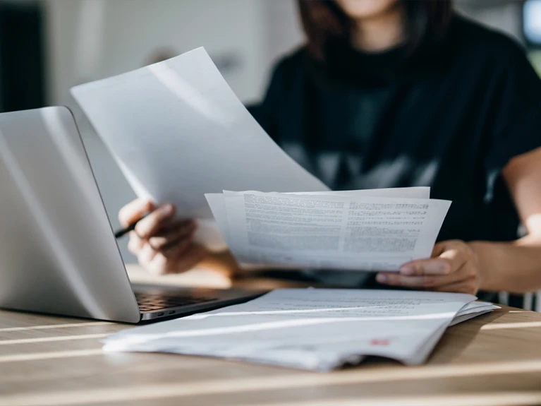 Person sitting at a table reading documents with a laptop beside them