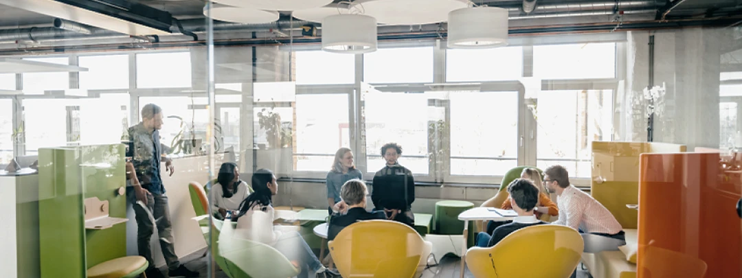 Modern office environment with several people sitting at colorful tables working or discussing