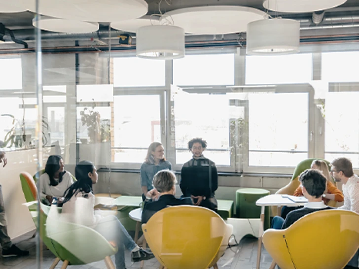 Modern office environment with several people sitting at colorful tables working or discussing