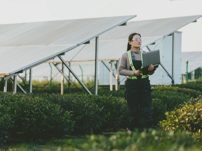 Technikerin mit Laptop prüft Solarpanelanlage im Feld