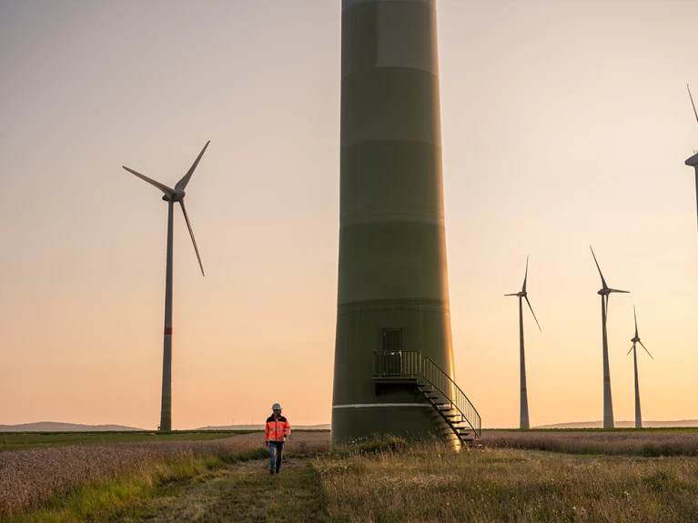 Person in Schutzkleidung untersucht Windrad bei Sonnenuntergang