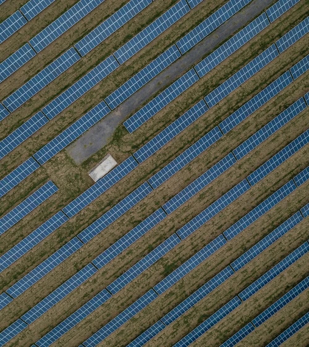 Luftaufnahme eines großen Solarparks mit gleichmäßig angeordneten Solarmodulen und einem kleinen Bereich mit Gras