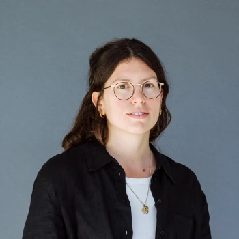 Portrait of a young woman wearing glasses and a black blouse against a grey background