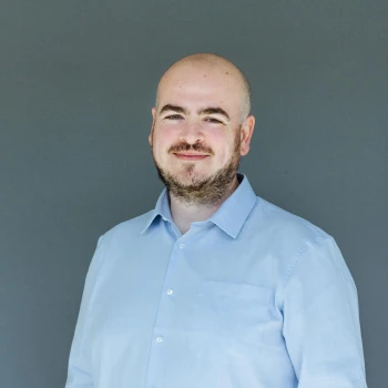 Portrait of a smiling bald man with a beard wearing a light blue shirt against a gray background