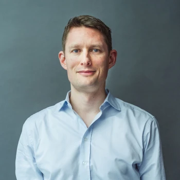 Portrait of a smiling man wearing a blue shirt against a gray background