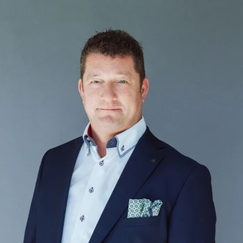 Portrait of a man with curly hair wearing a dark blue blazer with a pocket square and a white shirt