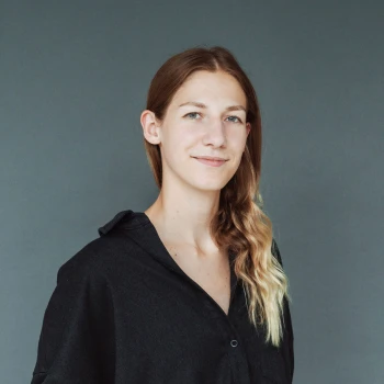 Portrait of a young woman with long, curly hair and a black shirt against a gray background