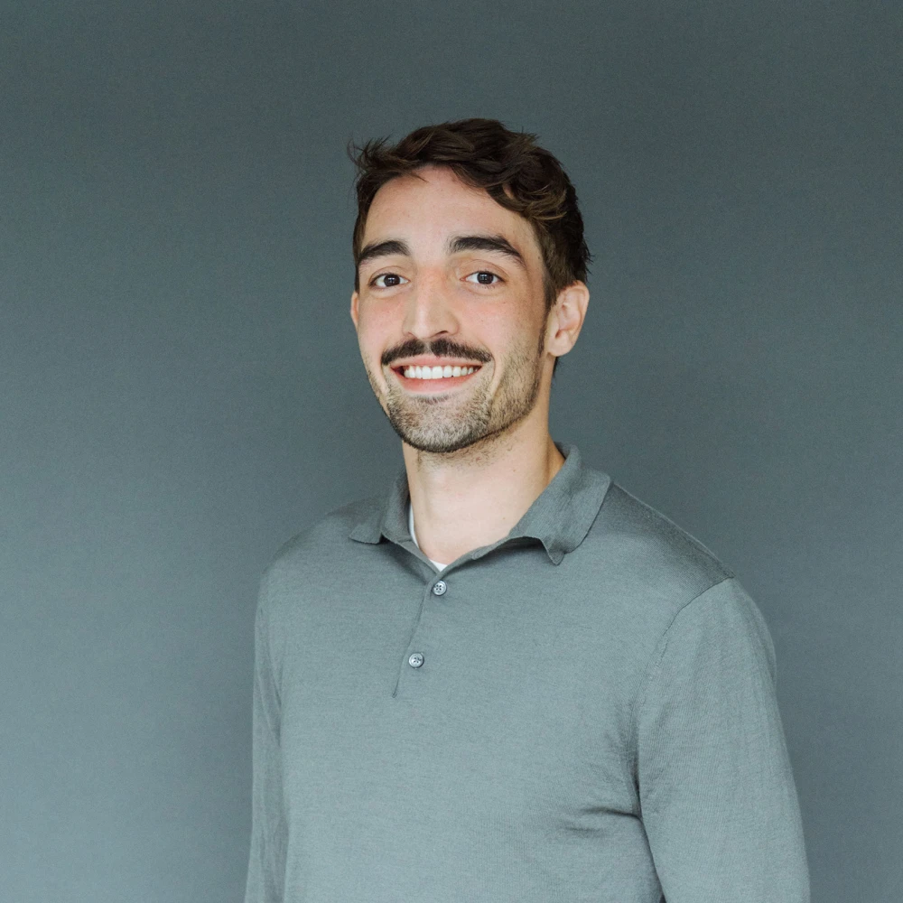 Porträt eines lächelnden Mannes mit Bart und grauem Poloshirt vor grauem Hintergrund