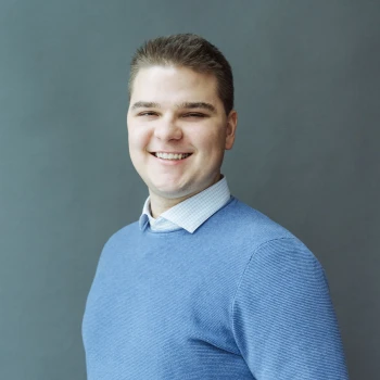 Portrait of a smiling young man in a blue sweater against a gray background