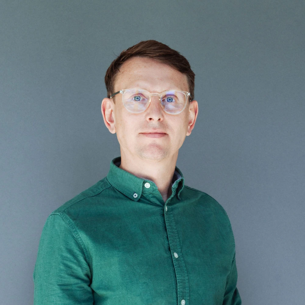 Porträt eines Mannes mit Brille und grünem Hemd vor grauem Hintergrund