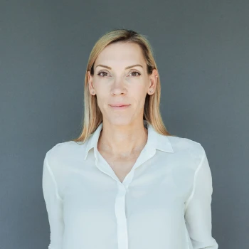 Portrait of a middle-aged woman with blonde hair and white blouse against a gray background