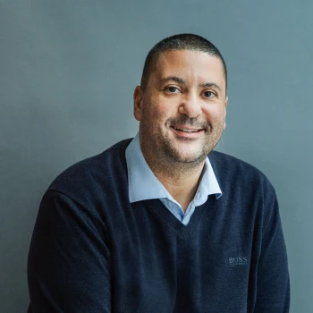Portrait of a smiling man wearing a dark sweater and shirt against a gray background