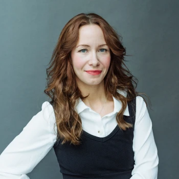 Portrait of a smiling woman with long curly hair wearing a white blouse and dark vest