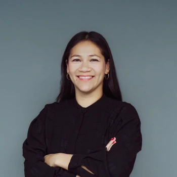 Portrait of a smiling Asian woman with crossed arms wearing a black top against a gray background